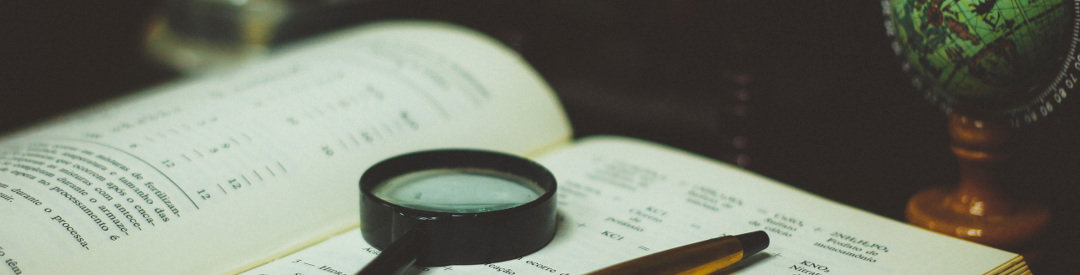 Book with magnifying glass and pen sitting on top, with a globe in the background